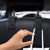 A hand is using black car seat back hooks to hang a white shopping bag for trunk organization.