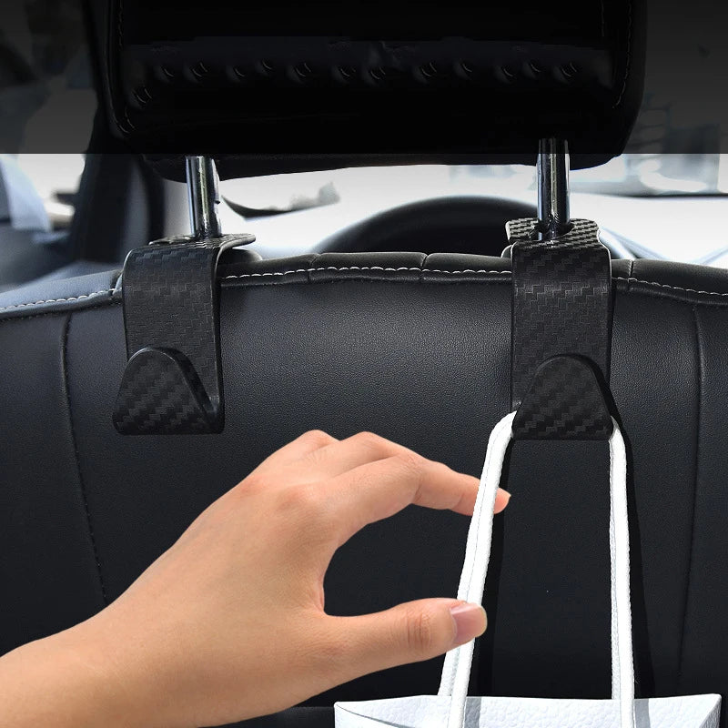 A hand is using black car seat back hooks to hang a white shopping bag for trunk organization.