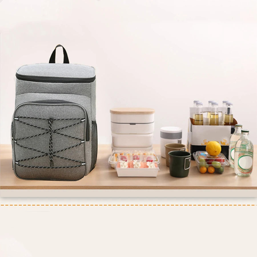 A gray insulated lunch backpack with a waterproof shell sits on a wooden surface next to various food items.