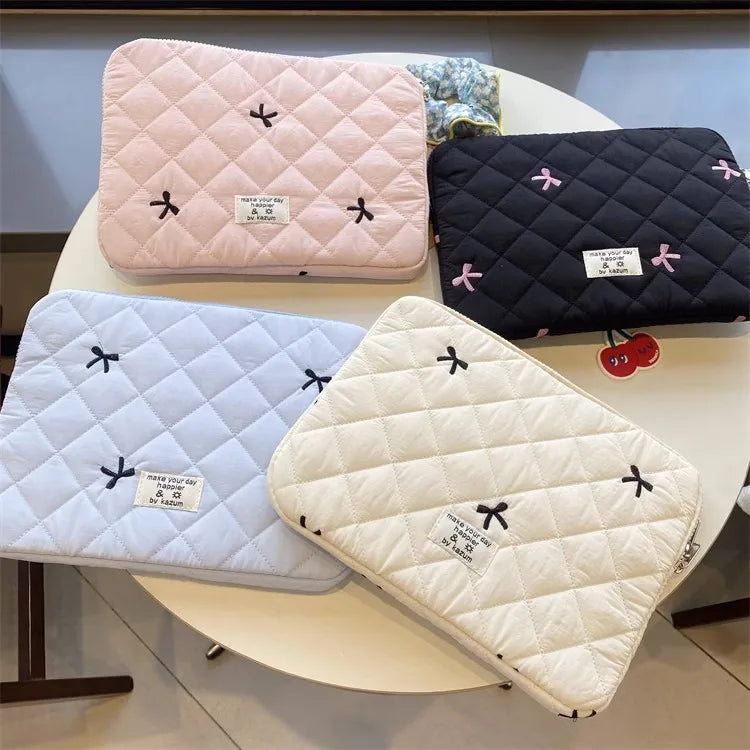 Three quilted laptop sleeves in pink, black, and cream fabric displayed on a white table.