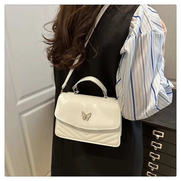 A woman is holding a white quilted shoulder messenger bag with a gold strap against a dark background.