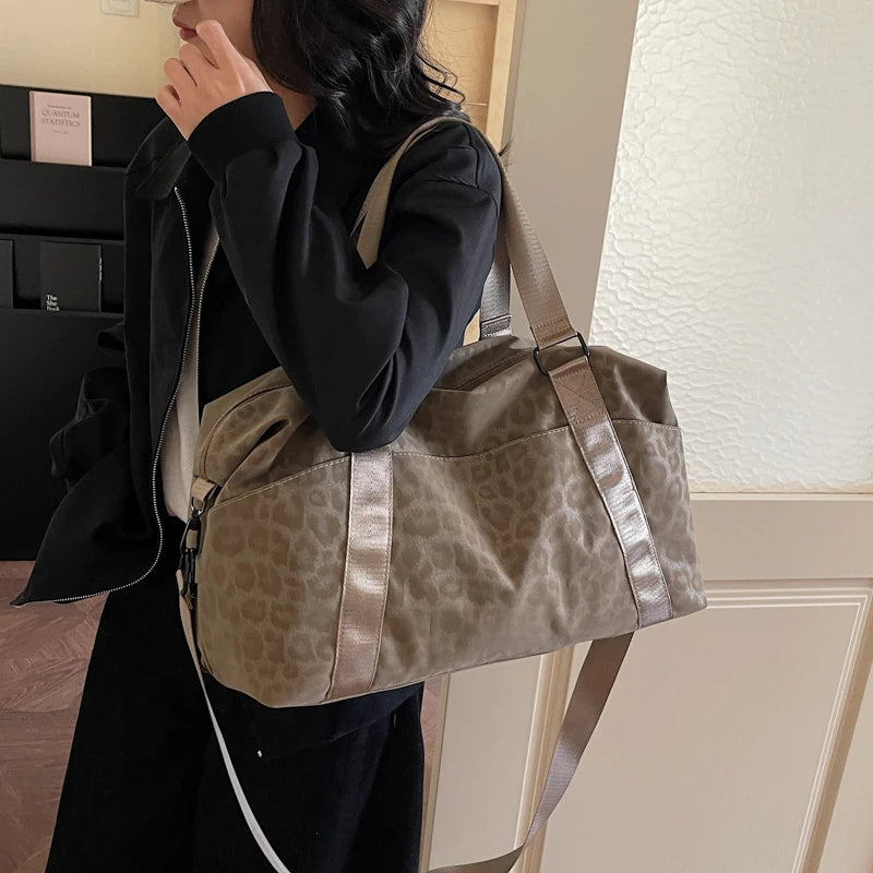 A woman holds a tan leopard print duffle bag with a leather strap against a light background.