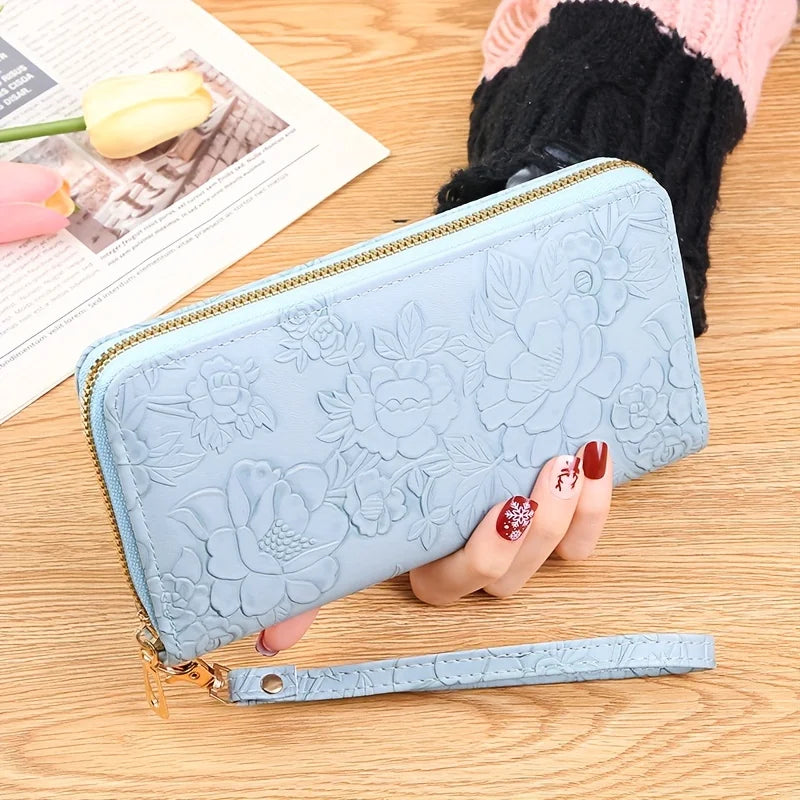 Cartera de tarjeta de cuero PU floral azul claro con cremallera dorada y correa de cuero sobre una superficie de madera.