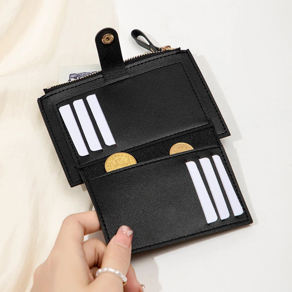 A black card holder wallet with silver stripes and gold accents is being held by a hand.