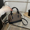 A black patterned fashion shell shoulder crossbody bag resting on a silver metal shelf.
