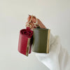 A hand holds a green fabric storage pouch with a red lining and gold keychain hardware.