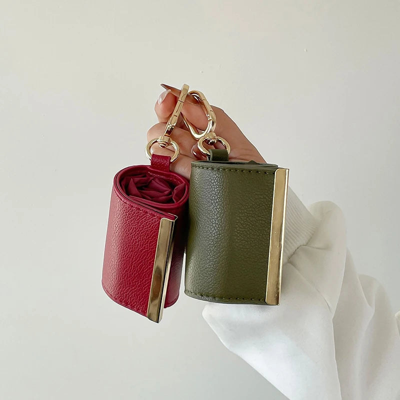 A hand holds a green fabric storage pouch with a red lining and gold keychain hardware.