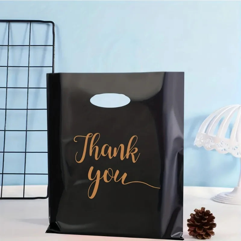 A black plastic gift bag with gold script text that reads Thank you is displayed next to a wire grid and a pine cone.