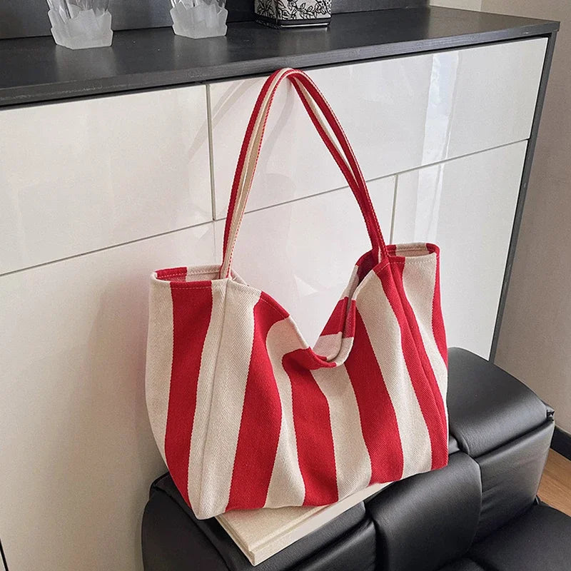 A red and white striped canvas tote bag with a handle is displayed on a dark surface.