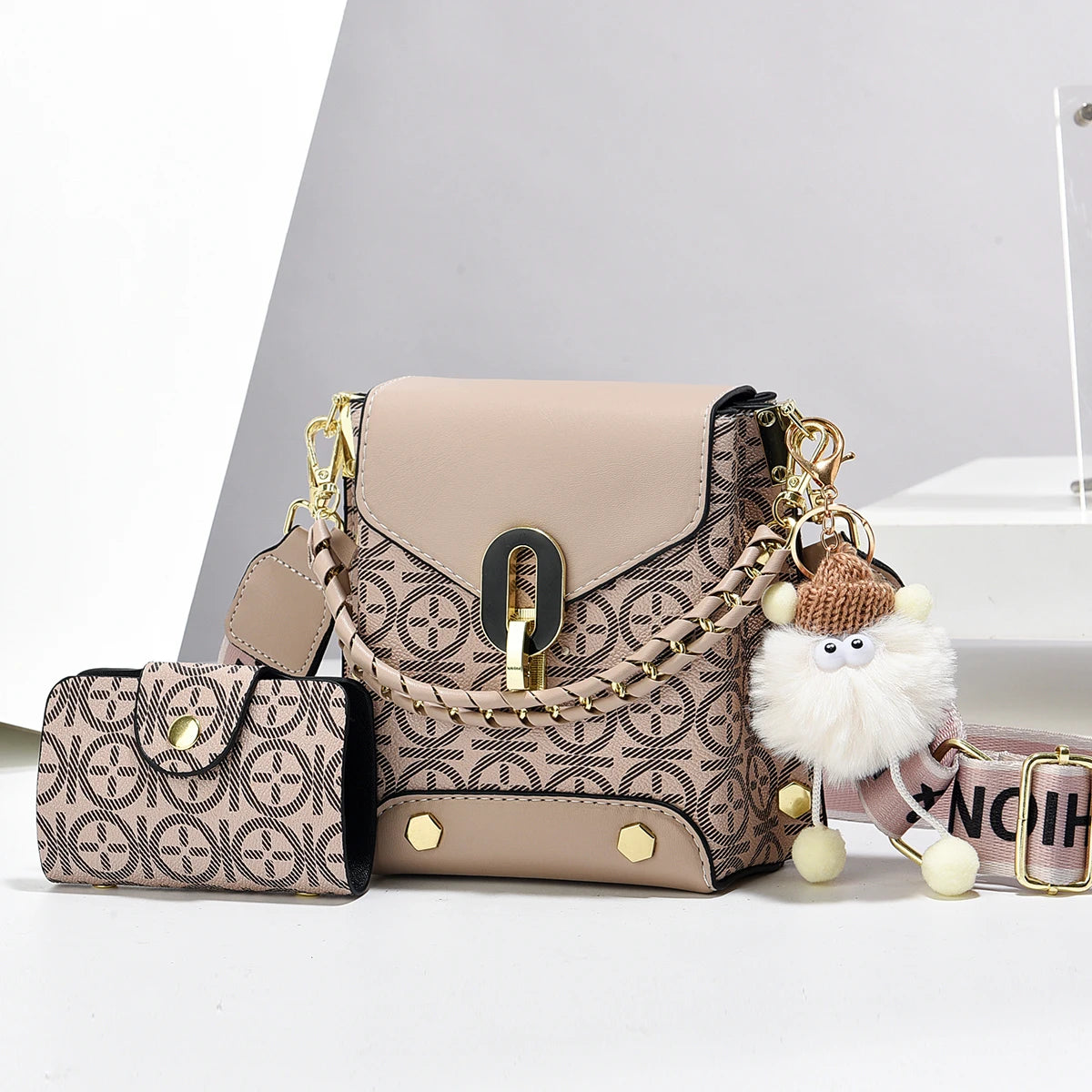 Sac bandoulière en similicuir beige avec détails de chaîne dorée et un charm pompon moelleux.