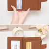 A brown leather wallet is shown open, displaying several credit cards and a coin pouch, held by a hand on a white surface.