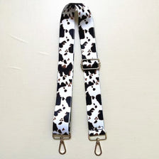 A black and white cow print textile replacement bag strap with gold-toned hardware.