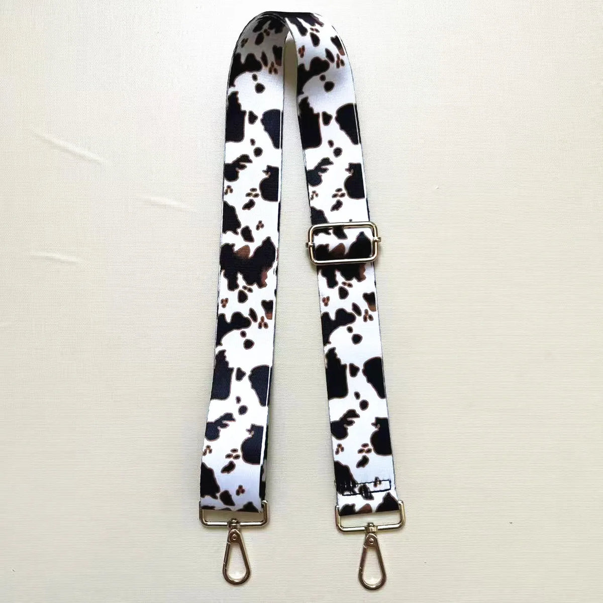 A black and white cow print textile replacement bag strap with gold-toned hardware.