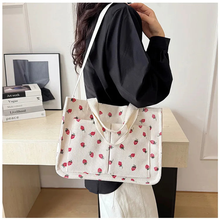A white canvas tote bag with a red strawberry pattern is held by a person against a light background.