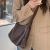 A woman holds a brown vintage PU leather tote bag with a dark brown crossbody strap against a light background.