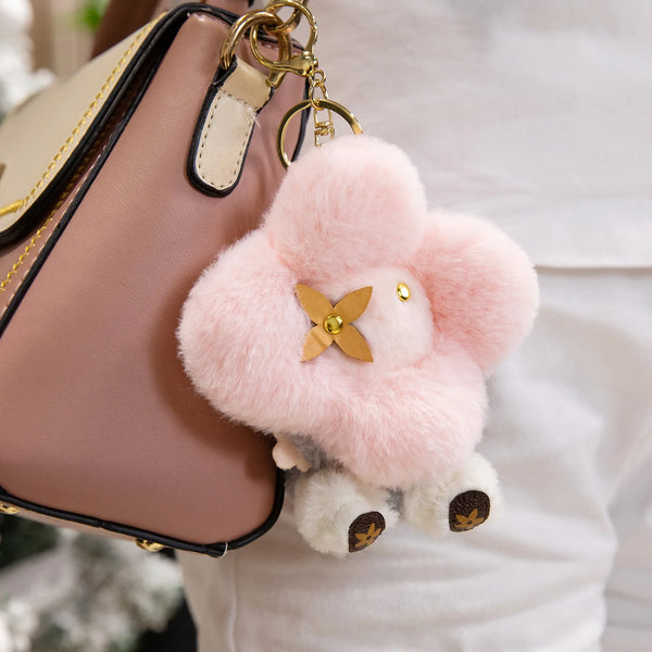 A pink and white fluffy sunflower plush keychain attached to a leather handbag.