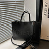 A black leather tote bag is displayed on a surface next to a window blind.