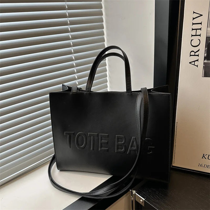 A black leather tote bag is displayed on a surface next to a window blind.