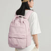 A woman wearing a beige cap holds a pink lightweight backpack for laptop and daily essentials.