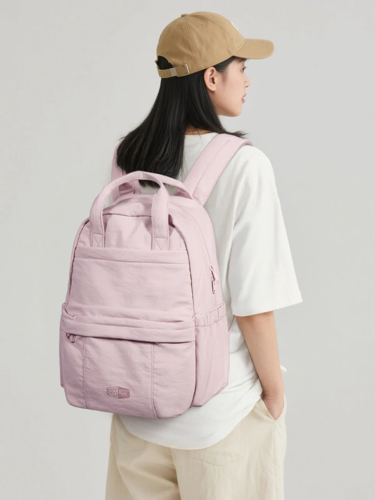 A woman wearing a beige cap holds a pink lightweight backpack for laptop and daily essentials.