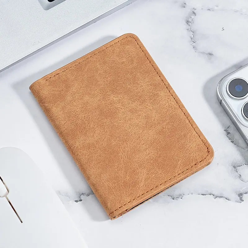 A tan leather card wallet is shown resting on a white marble surface next to a silver electronic device.