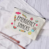 A cream-colored pouch labeled Emergency Snacks with colorful illustrations of candies and snacks, resting on a white cloth.