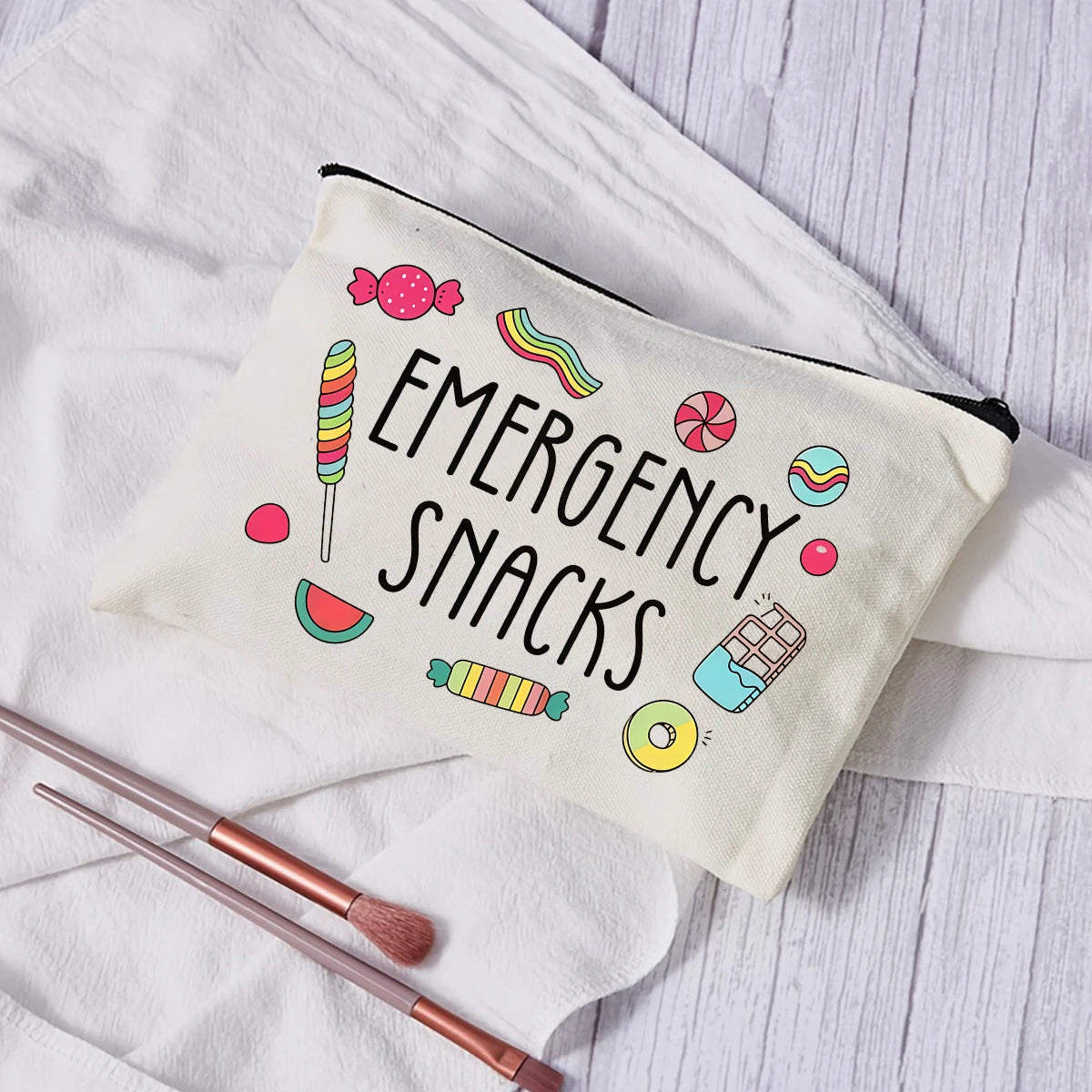 A cream-colored pouch labeled Emergency Snacks with colorful illustrations of candies and snacks, resting on a white cloth.