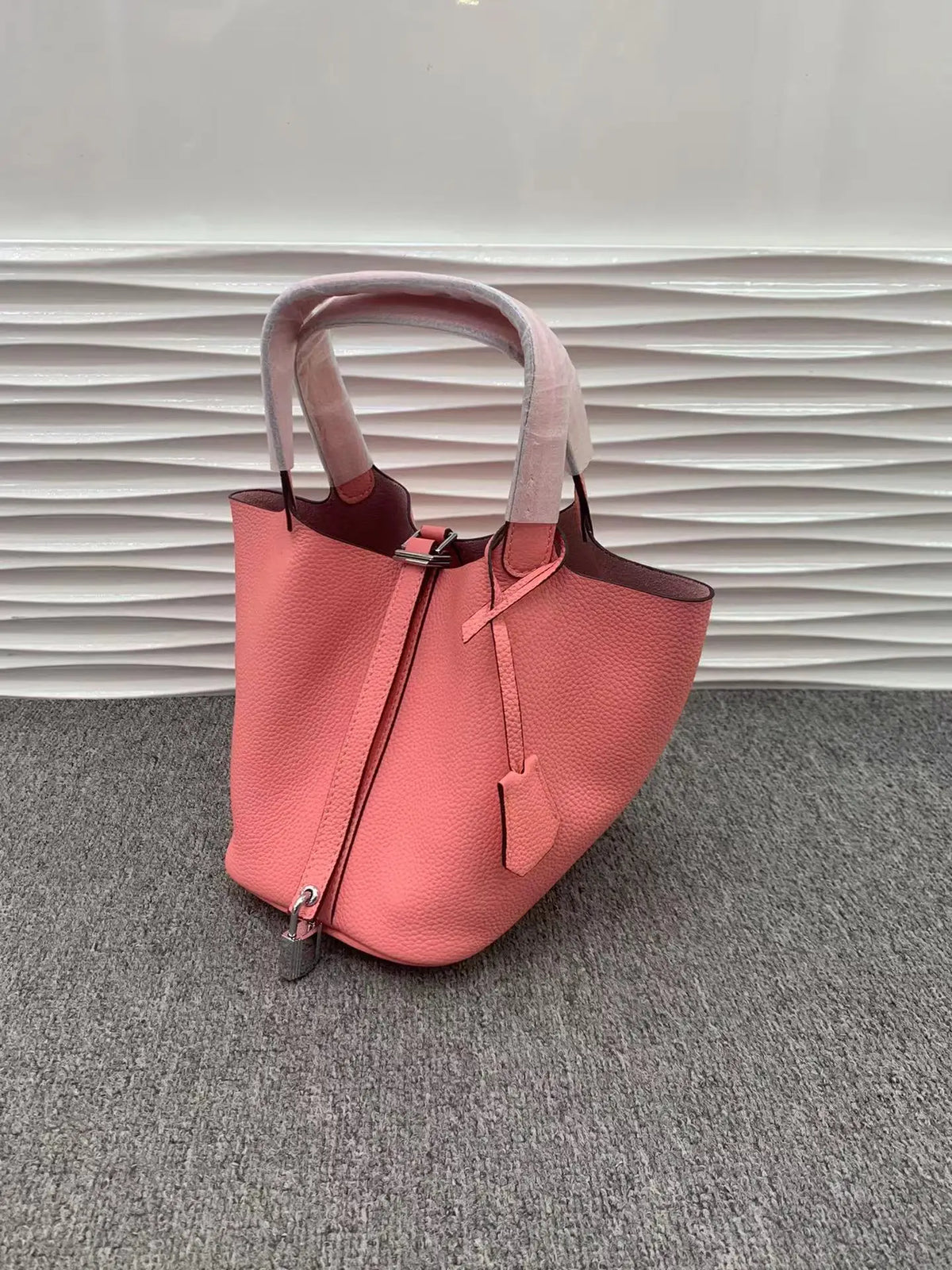 Pinkes Leder-Bucket-Bag mit rosa Träger auf grauem Untergrund.