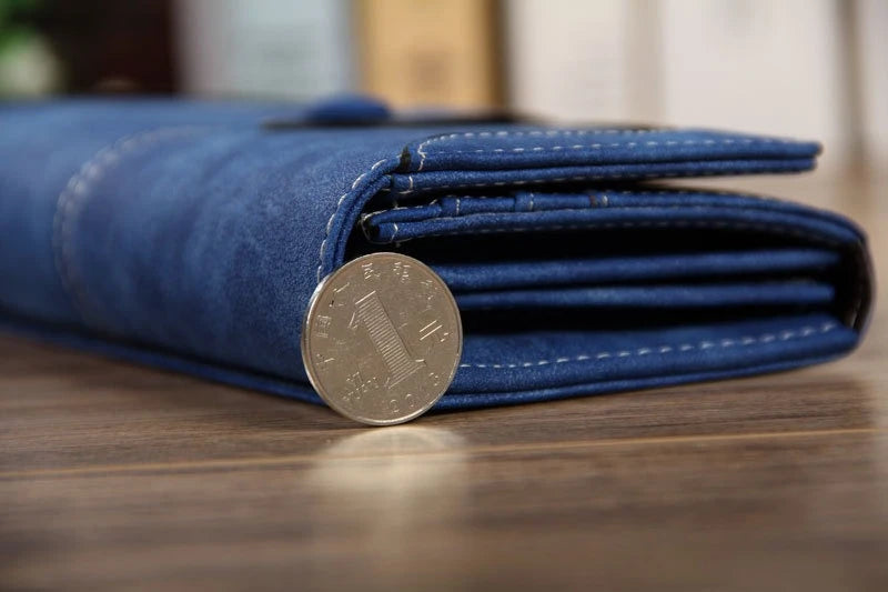 A dark blue leather clutch wallet folded and displaying a coin.