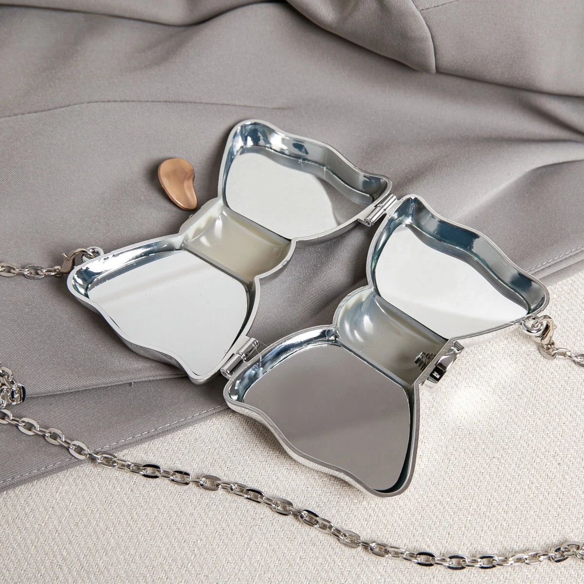 Silver acrylic bow clasp mini handbag with a chain strap resting on a gray fabric.