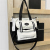 Schwarze und weiße Nylon-Eimertasche mit schwarzen Riemen, an einem hellen Holzregal hängend.