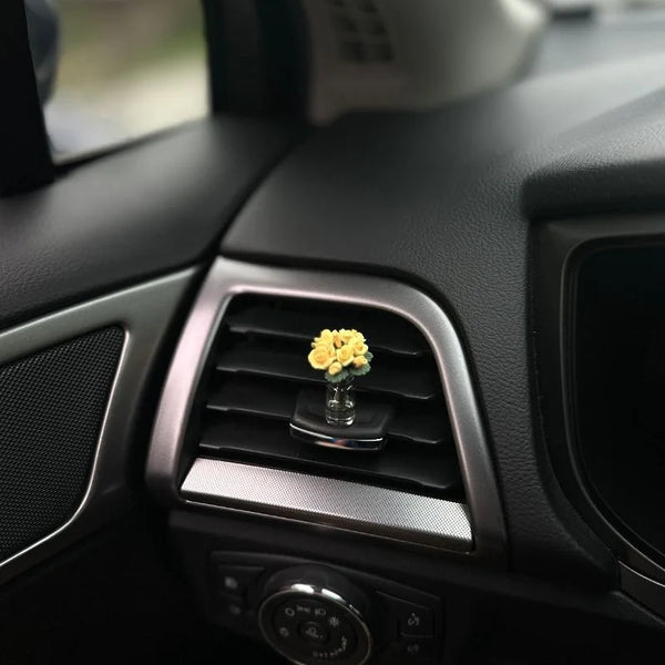 Vue rapprochée de l'intérieur d'une voiture montrant un vase décoratif avec des roses jaunes dans un conduit d'aération.