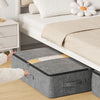 A gray foldable underbed storage bag is placed on a wooden floor next to a white bed frame.