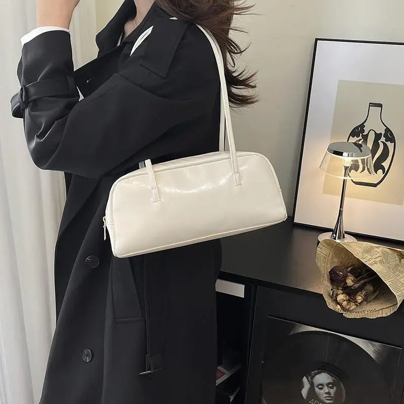 A woman wearing a black coat holds a cream glossy PU leather tote bag with dual straps.
