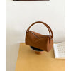 A tan faux suede crossbody bag resting on a light wood surface next to a book.