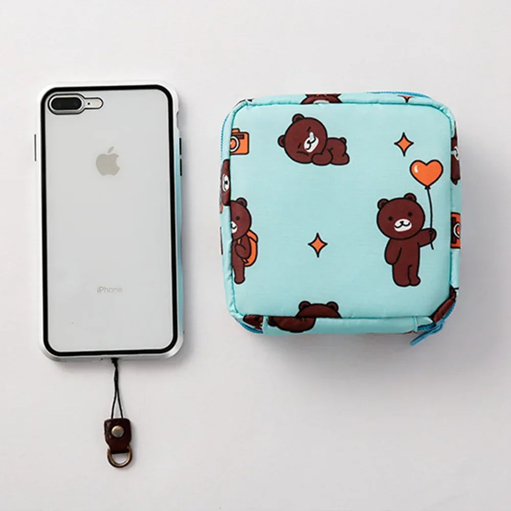 A light blue fabric pouch with a pattern of cute brown bears and orange hearts, next to an iPhone.