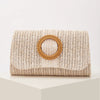 A beige woven straw envelope clutch with a round leather detail sits on a white surface.