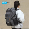 A person is shown wearing a small gray travel backpack with a black rain cover.