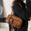 Bolso de hombro de cuero sintético marrón retro con herrajes dorados llevado por una persona con un abrigo negro.