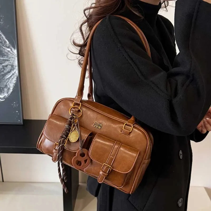 Bolso de hombro de cuero sintético marrón retro con herrajes dorados llevado por una persona con un abrigo negro.