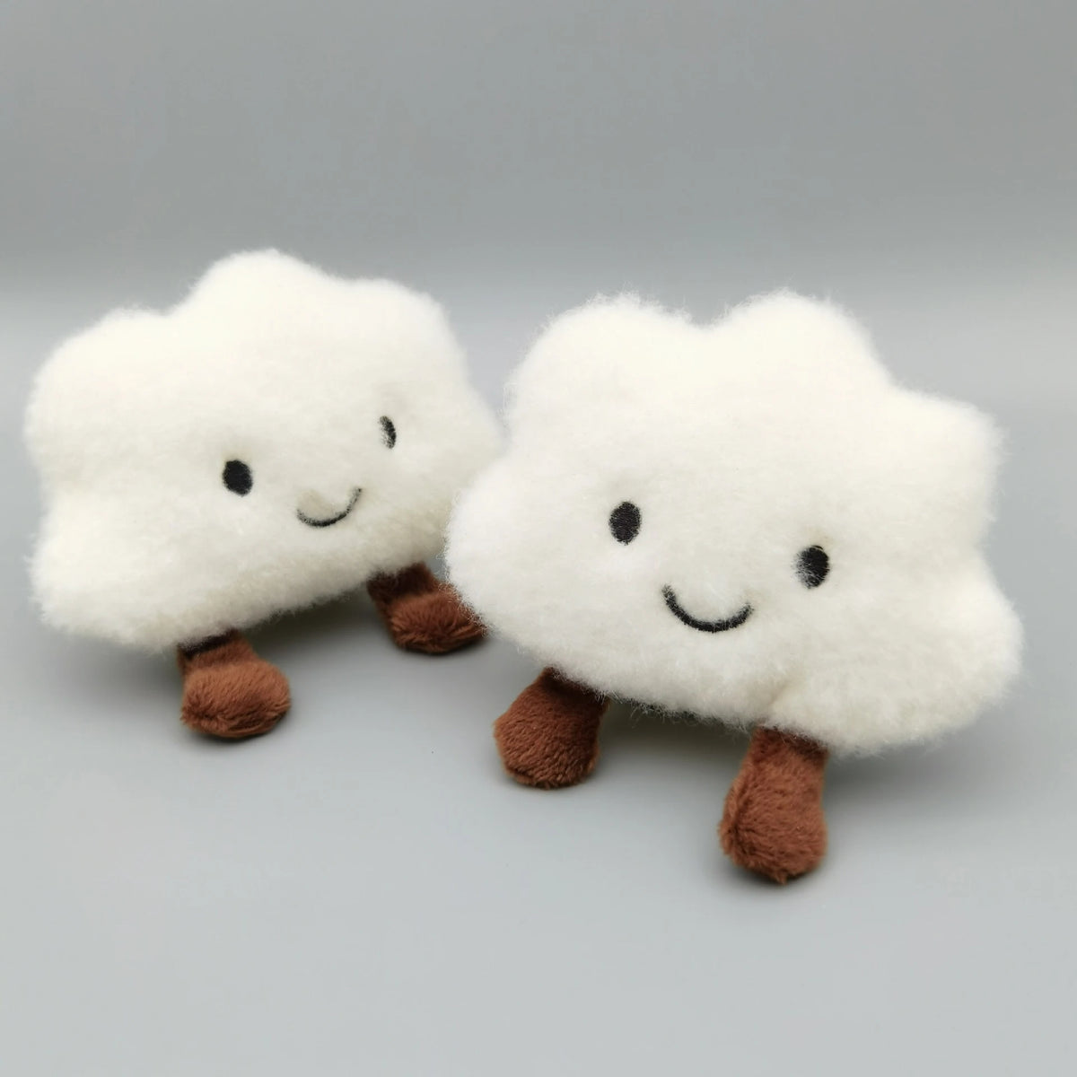 A pair of white fluffy cloud-shaped plush keychains with brown feet.