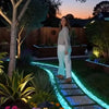 A woman stands on a glowing pathway made of illuminated pebbles in a garden setting.