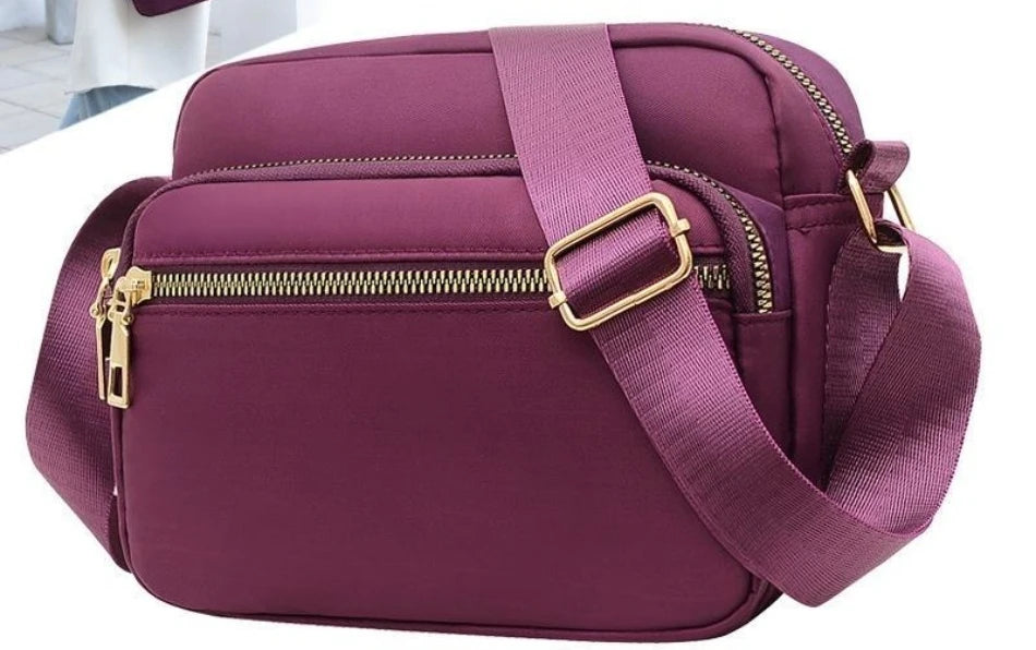 A deep purple compact oxford fabric crossbody bag with a gold-toned zipper and strap.