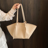 A light beige luxury PU leather shoulder tote bag is being held by a person against a dark wooden background.