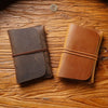 Two brown leather passport holders or card wallets resting on a wooden surface.