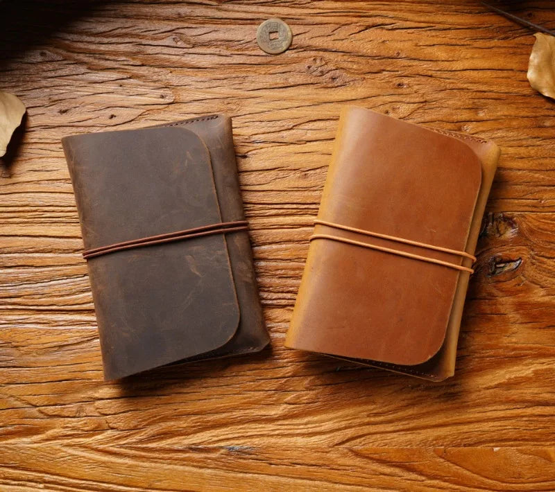 Two brown leather passport holders or card wallets resting on a wooden surface.