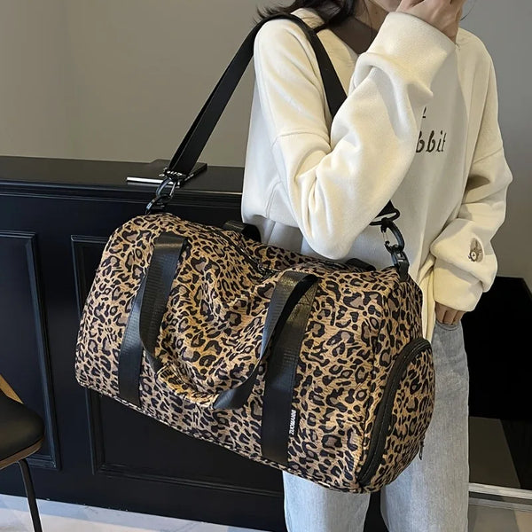 A person is holding a leopard print travel tote bag with a shoe compartment.