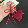 A red faux fur charm keychain with a leopard print heart and pearl beads is displayed on a hand.