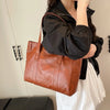 Eine Frau hält eine braune Vintage-PU-Leder-Handtasche gegen einen hellen Hintergrund.