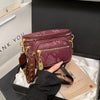 A maroon riveted waist bag with gold hardware is displayed in a black box on white fabric.